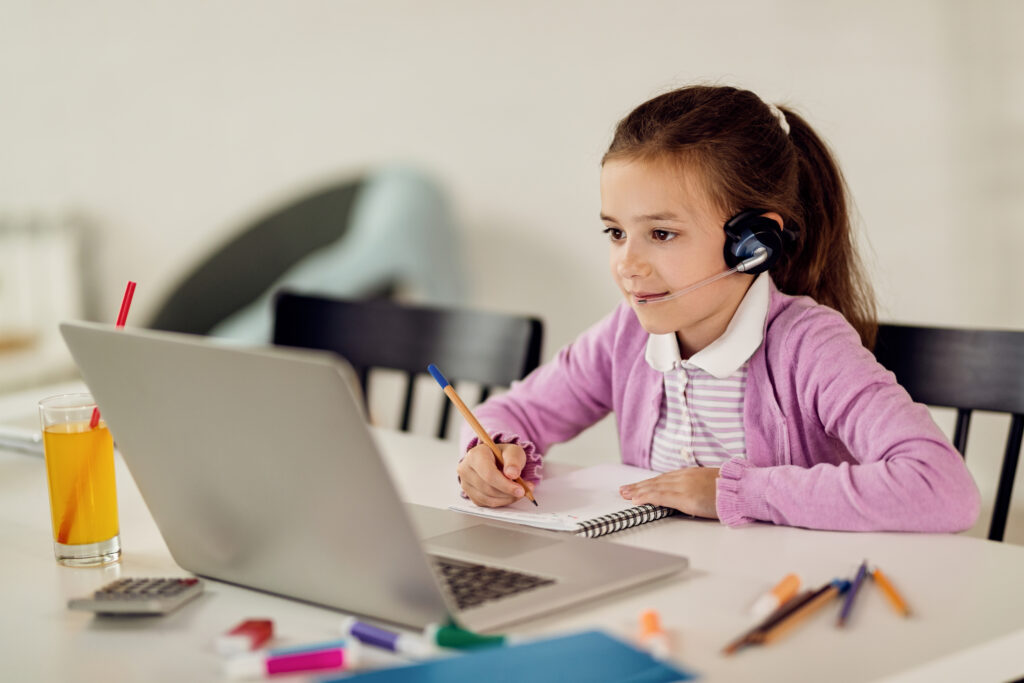 Cute girl writing notes while e-learning over laptop at home.